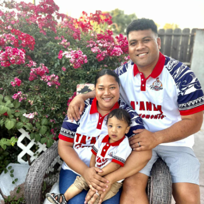 A family of three wearing matching red, white, and blue tops. A small child in the middle is being held by a woman. A man is to the right holding the woman.