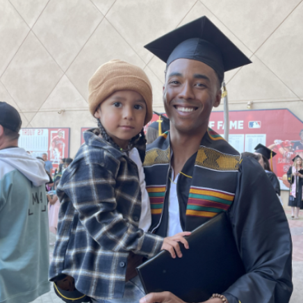 A man holding a small child and wearing graduation attire