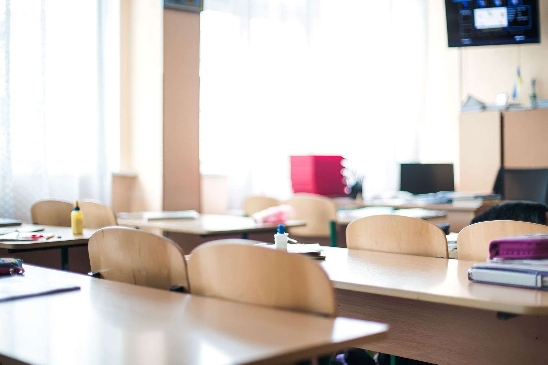 A classroom with tables and chairs and a television on the wall.