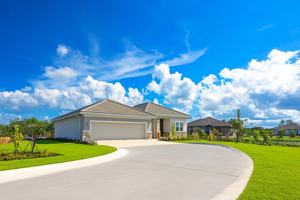 House with a curved driveway, surrounded by green lawn under a bright blue sky with fluffy white clouds.
