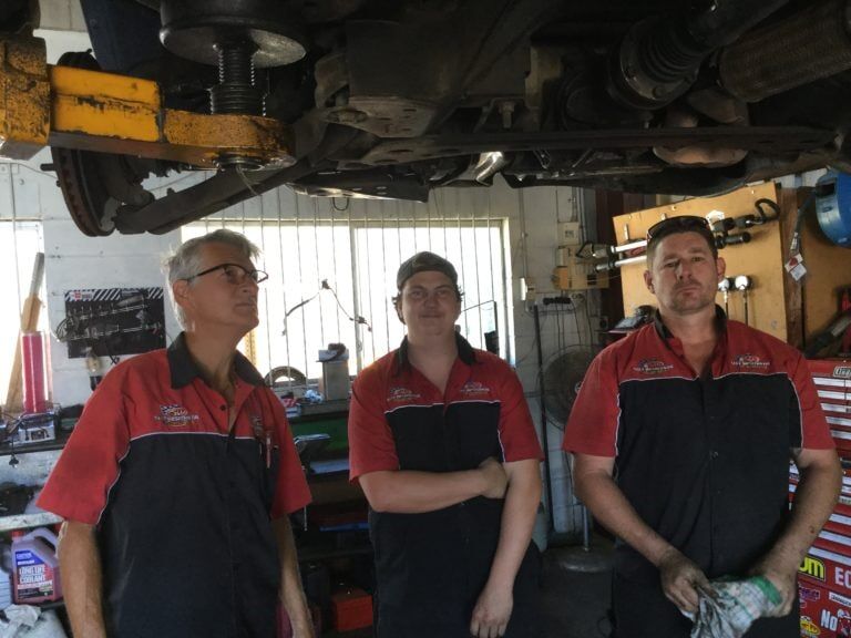 Three men are Standing Under a car in a Garage — Mechanical Servicesin Maroochydore, QLD