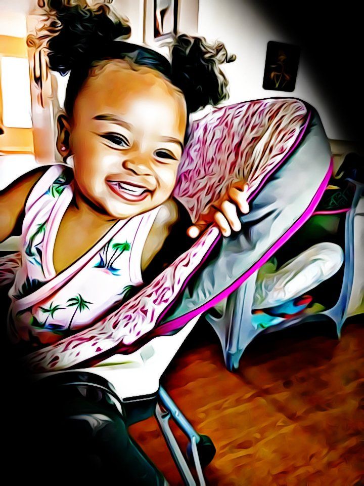 A baby girl is sitting in a high chair and smiling.