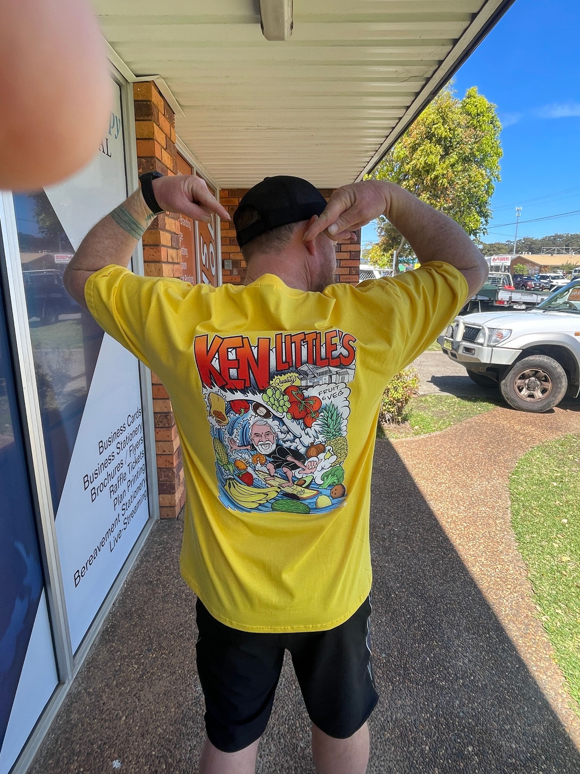 Person in yellow t-shirt with graphic, pointing at the back. Outdoors, sunny day — Carbon Copy in Port Macquarie, NSW