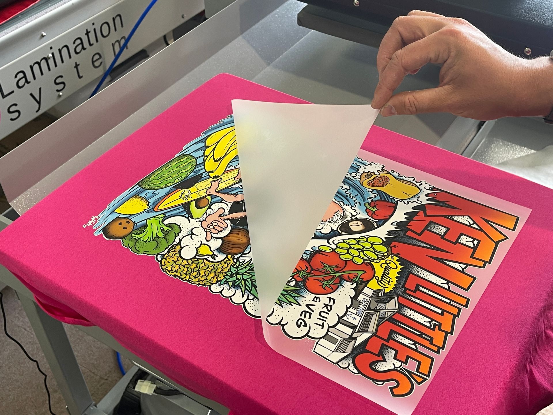 Person peeling a protective sheet from a colorful printed design on a pink t-shirt. — Carbon Copy Digital in Port Macquarie, NSW