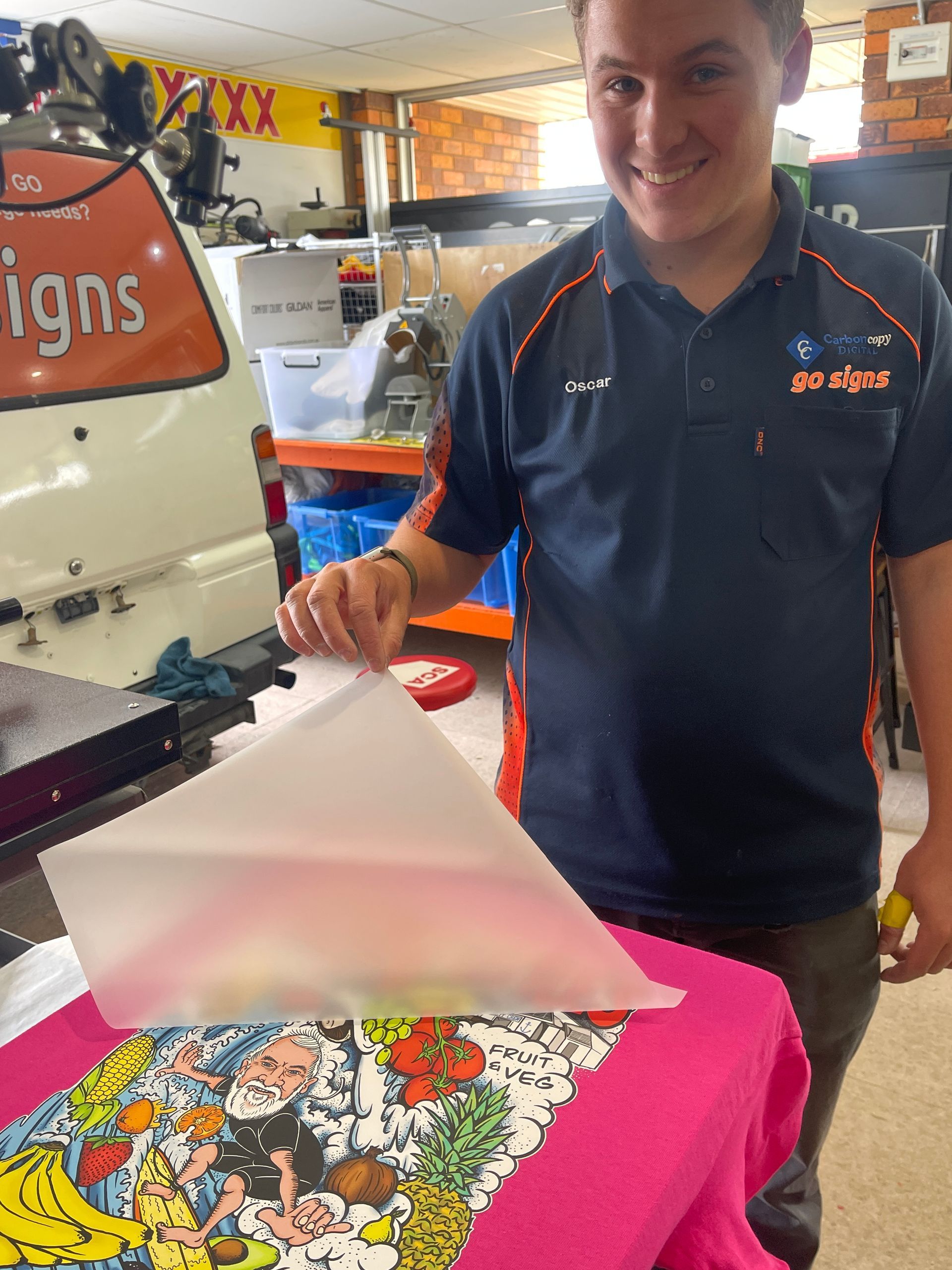 Man peeling paper from a colorful print on a pink shirt, standing in a print shop. — Carbon Copy Digital in Kempsey, NSW