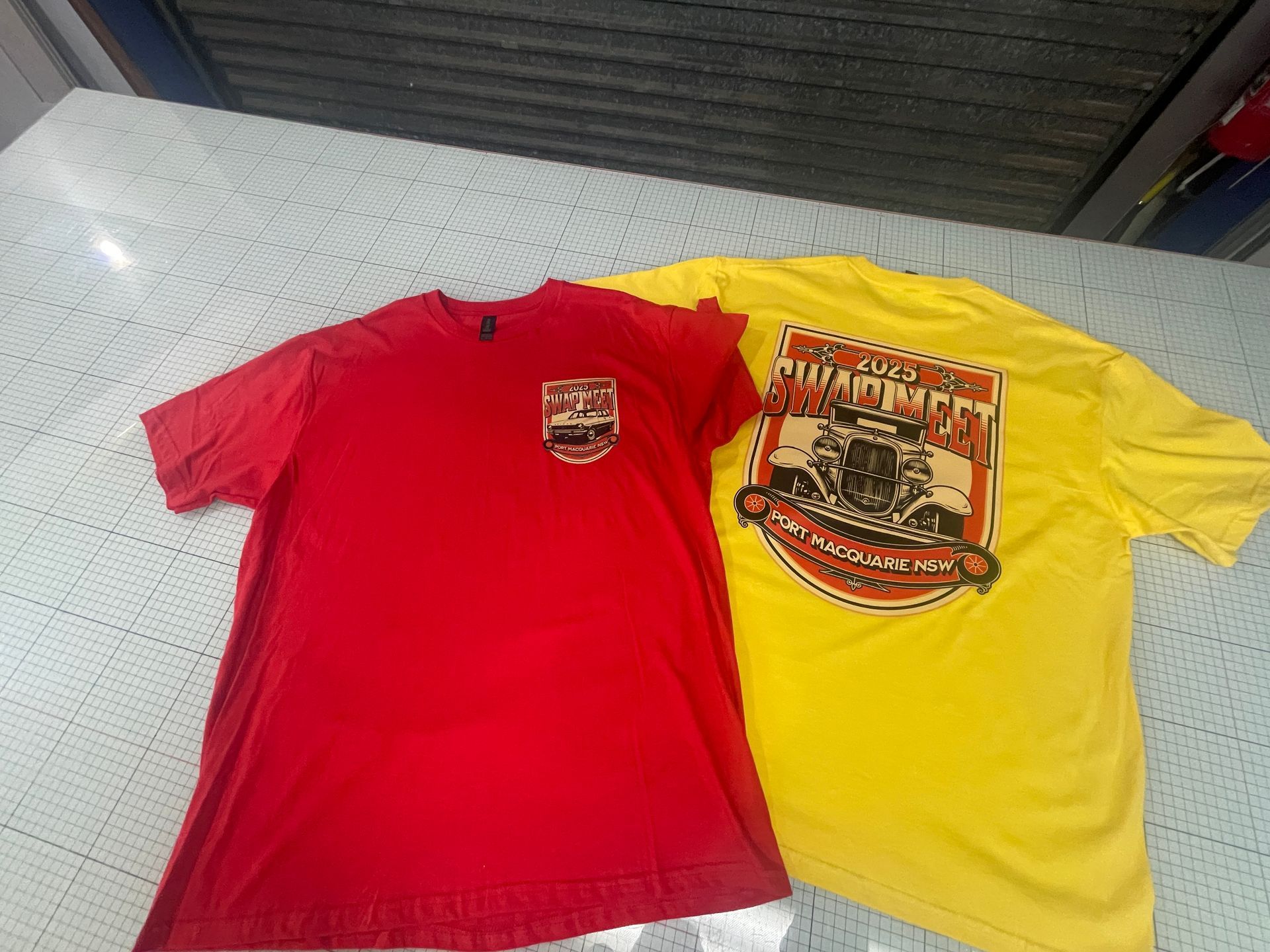 Two t-shirts: Red and yellow, both with a crest design featuring a car — Carbon Copy in Port Macquarie, NSW