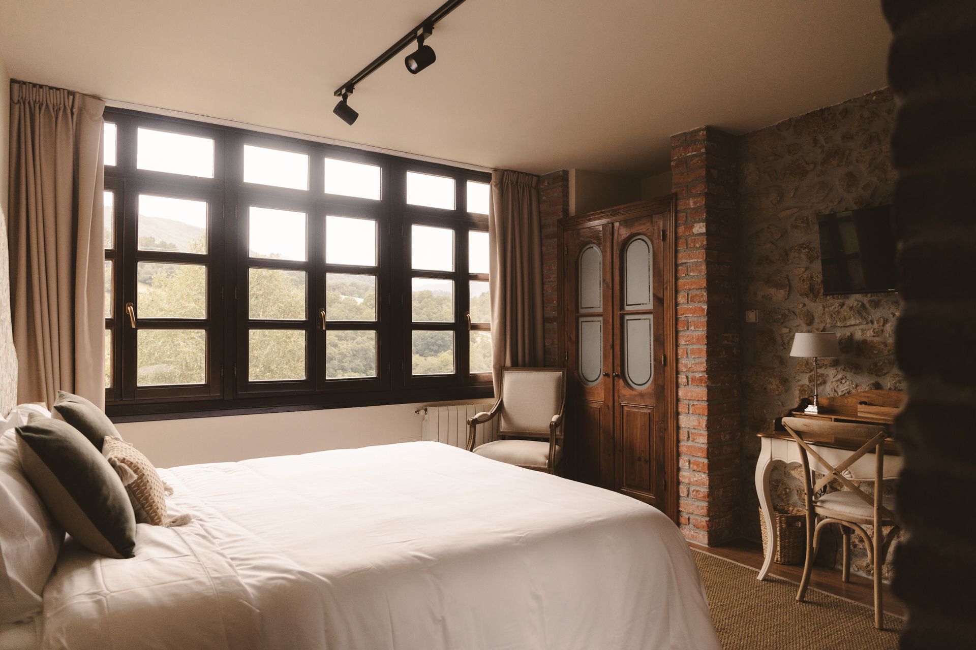 A bedroom with a large bed , chair , desk and window.