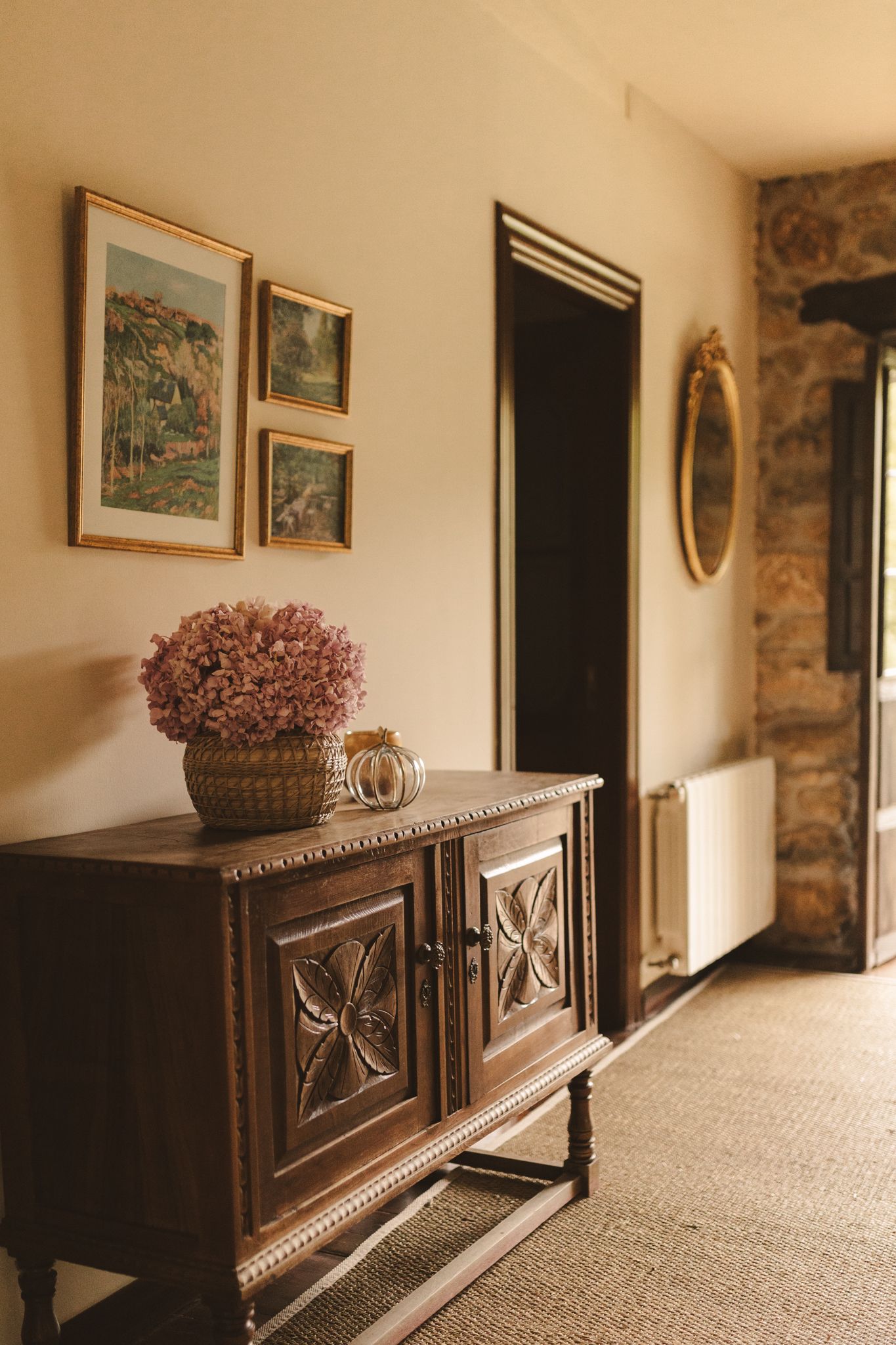 A wooden dresser with a vase of flowers on top of it in a hallway.