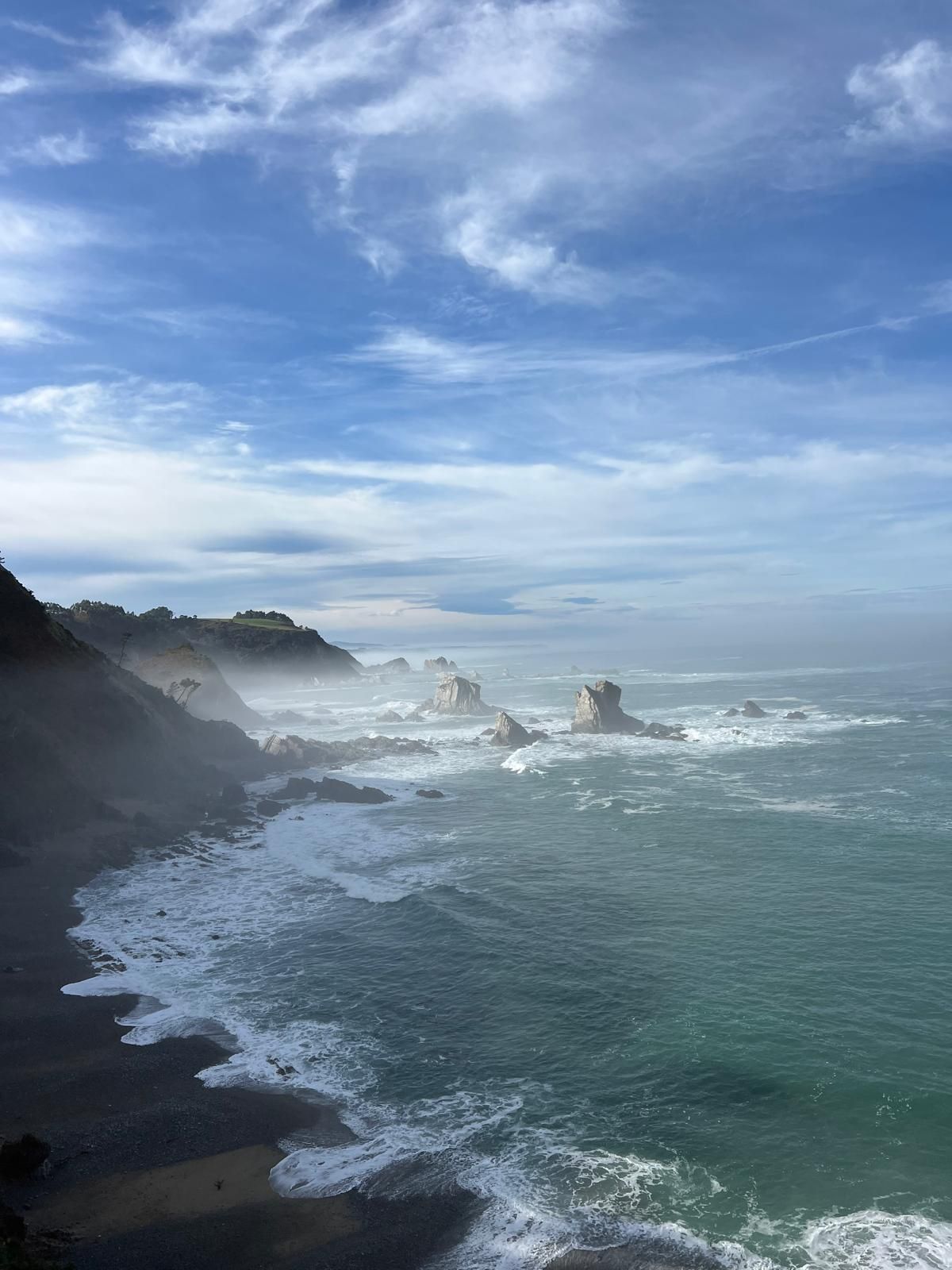 A view of the ocean from a cliff on a cloudy day.