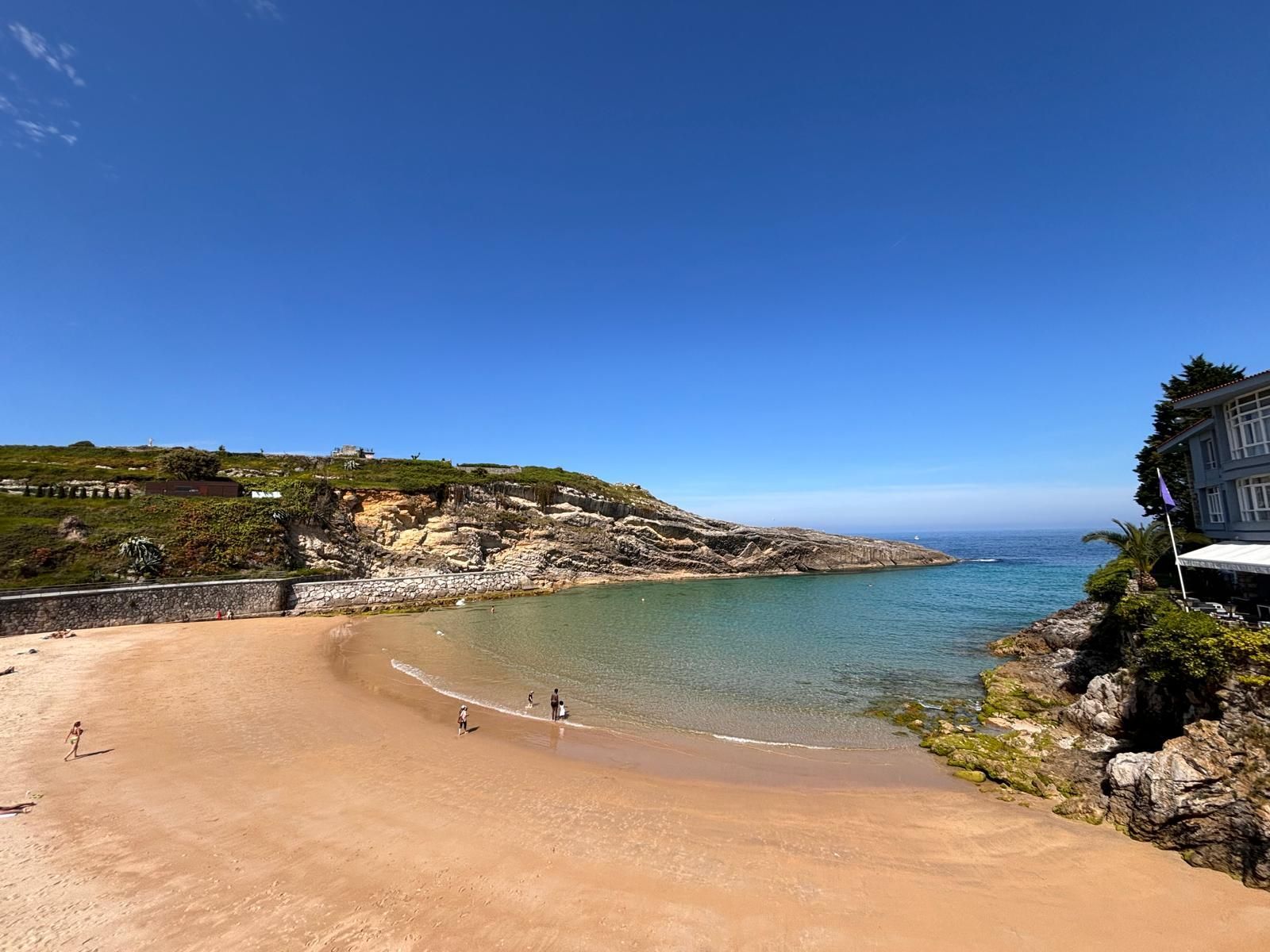 A beach with a house in the background and a blue sky