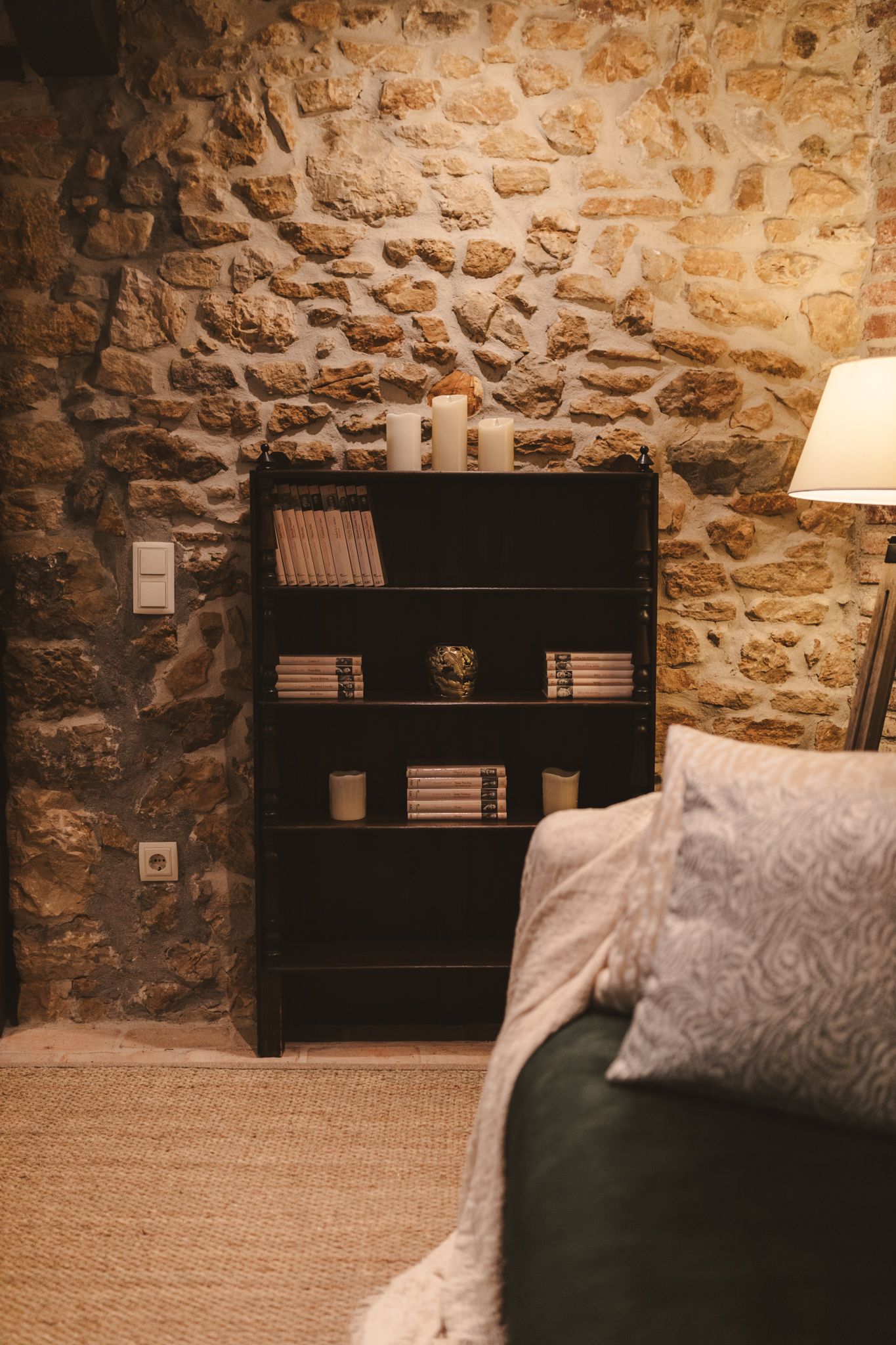 A living room with a stone wall , a couch , a lamp and a bookshelf.