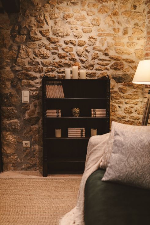 A living room with a stone wall , a couch , a lamp and a bookshelf.