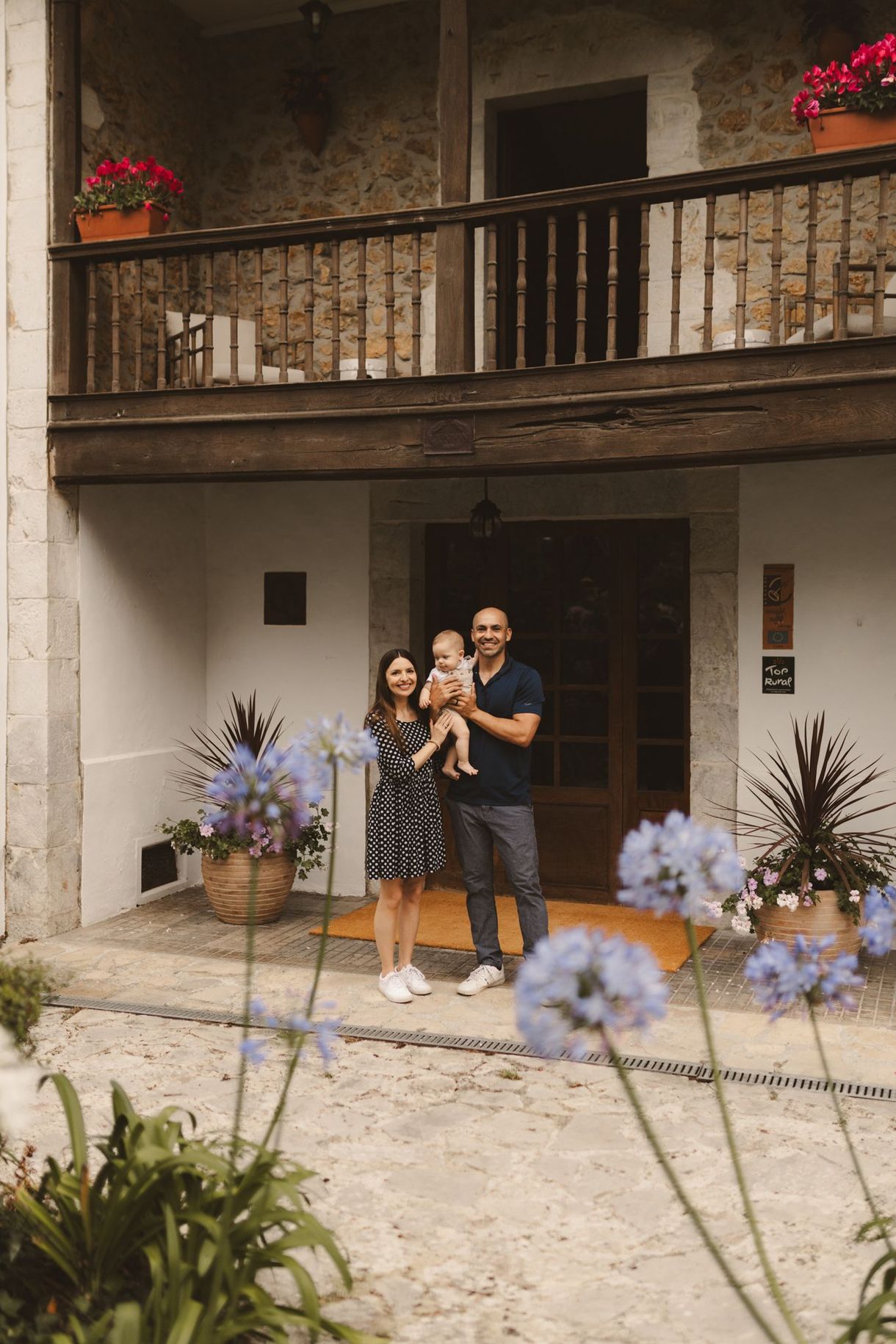 A man and woman are holding a baby in front of a house.