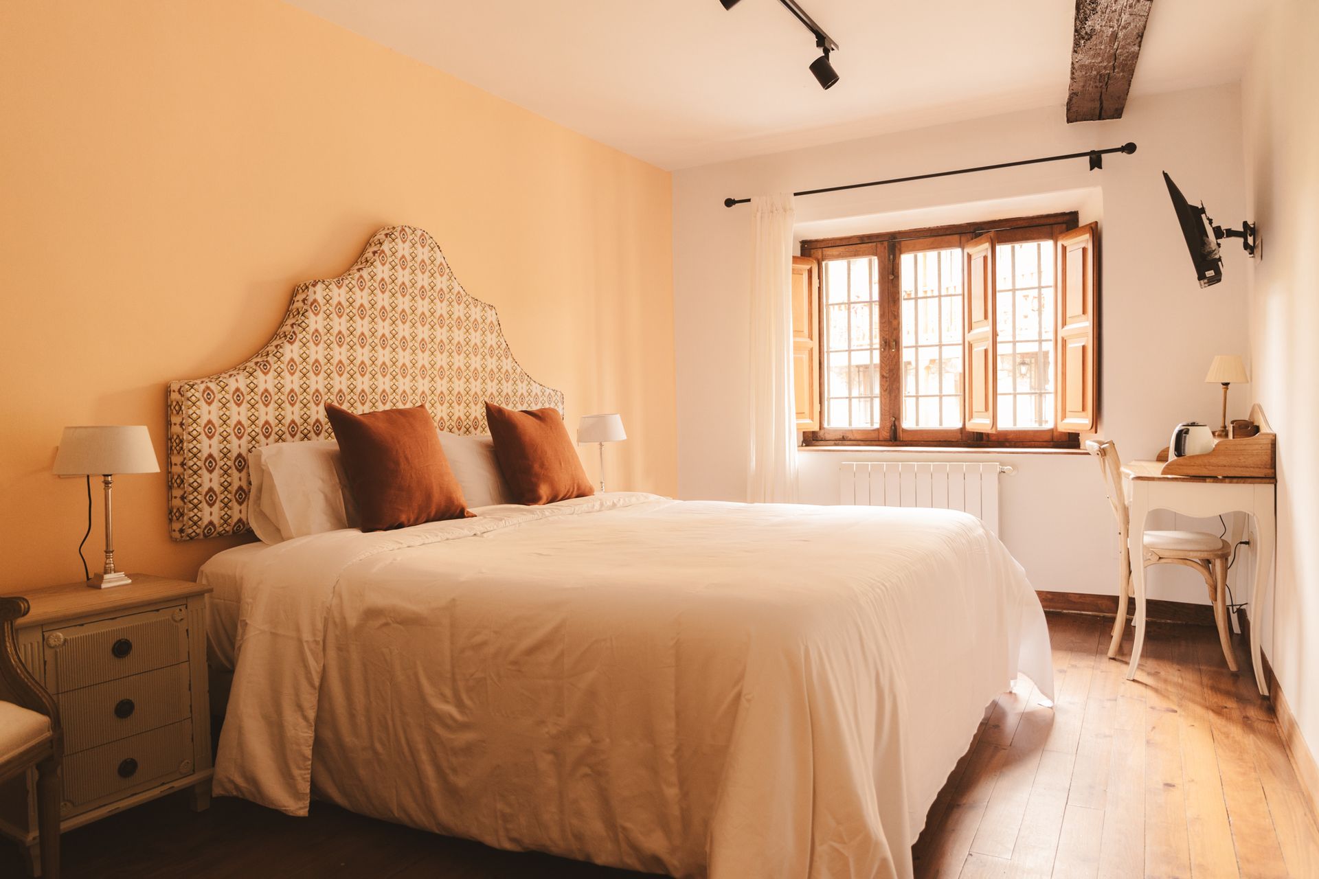 A bedroom with a large bed , two nightstands , a desk and two windows.