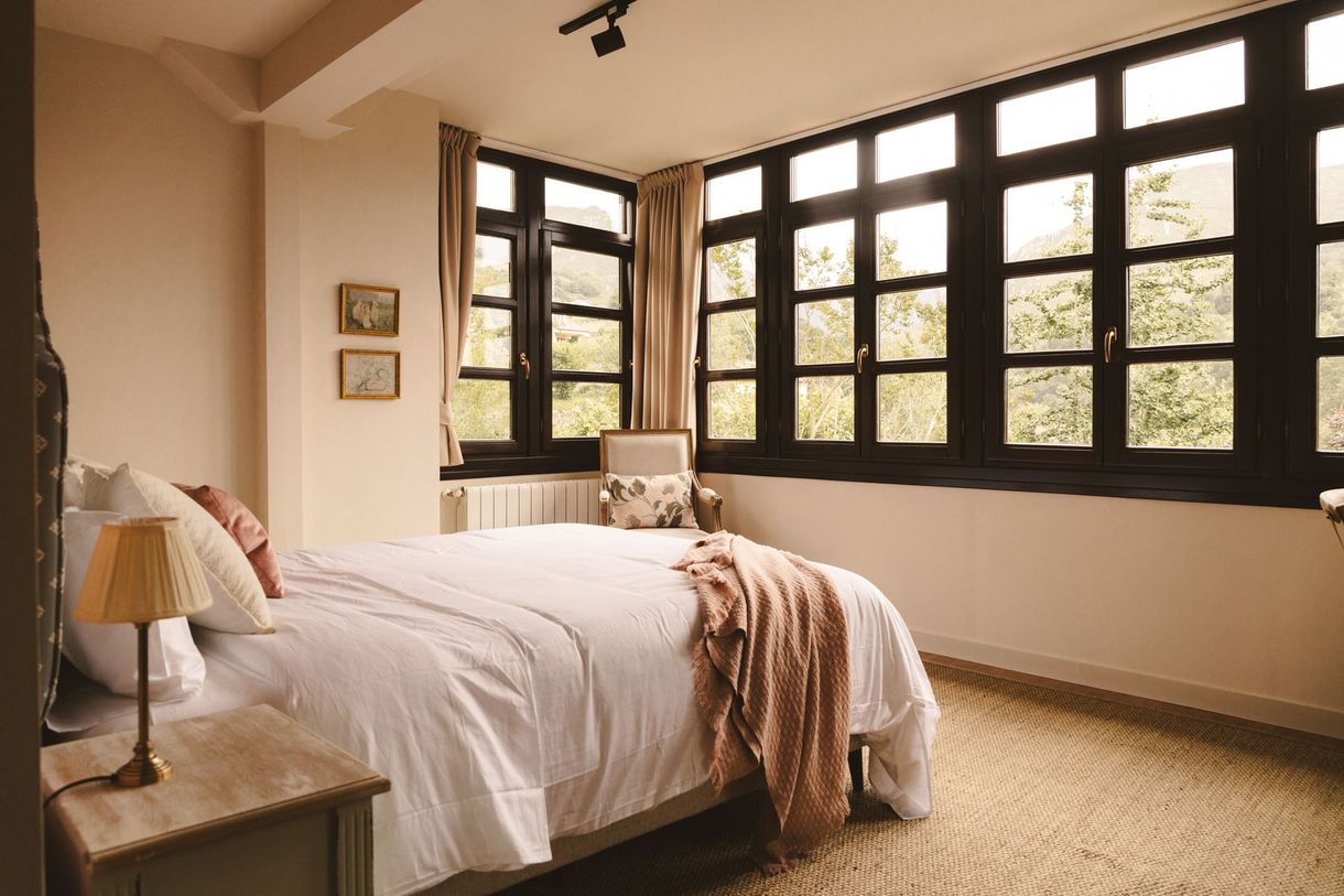 A bedroom with a bed , chair , nightstand and lots of windows.