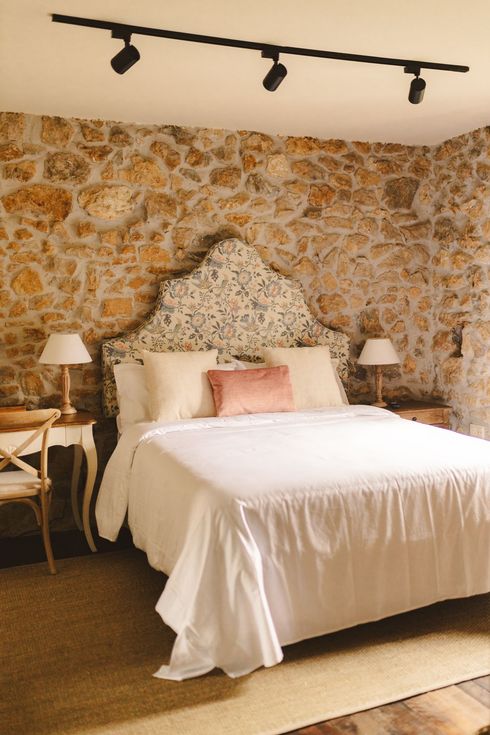 A bedroom with a bed , lamps , and a stone wall.