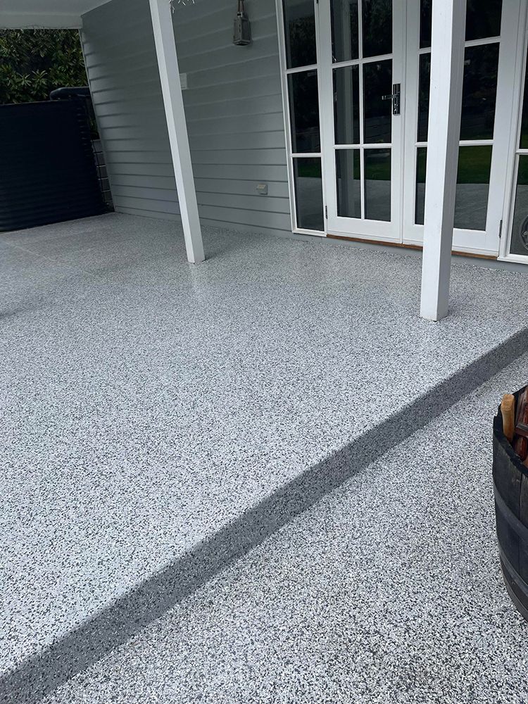 A patio with a concrete floor and a white house in the background
