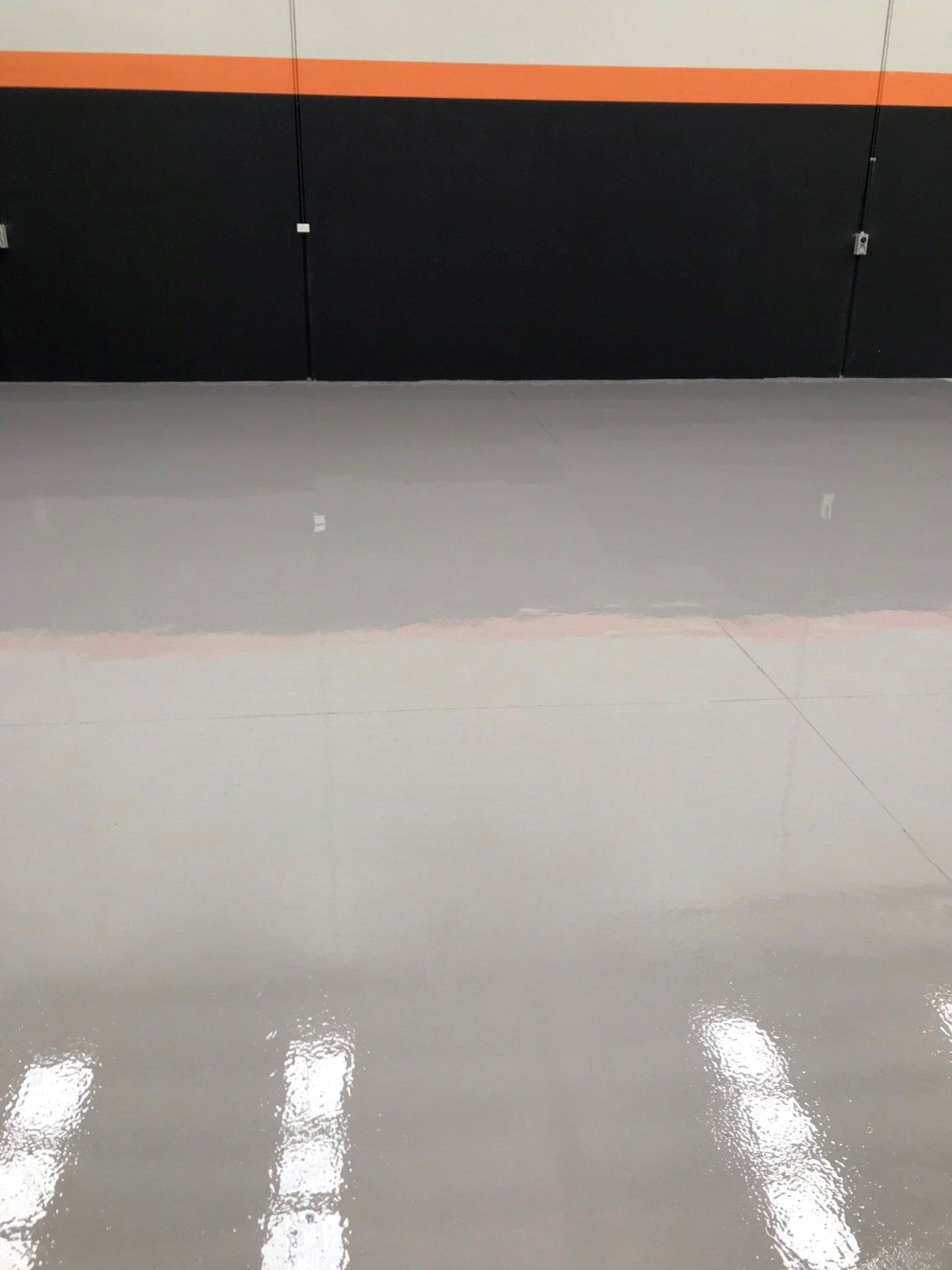 A large empty room with a concrete floor and a black and orange wall