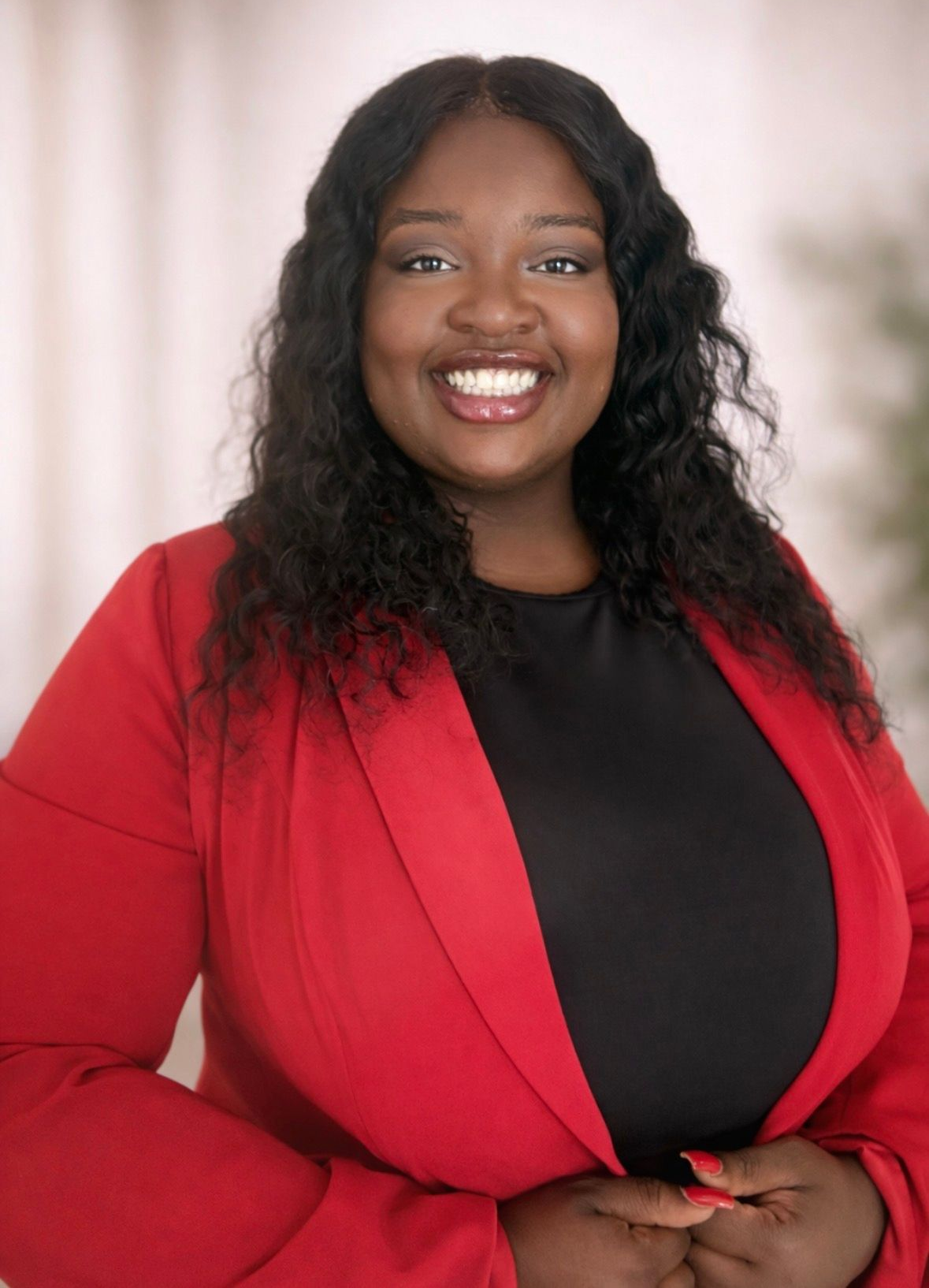 Smiling person in a red blazer and black top against a soft blurred background