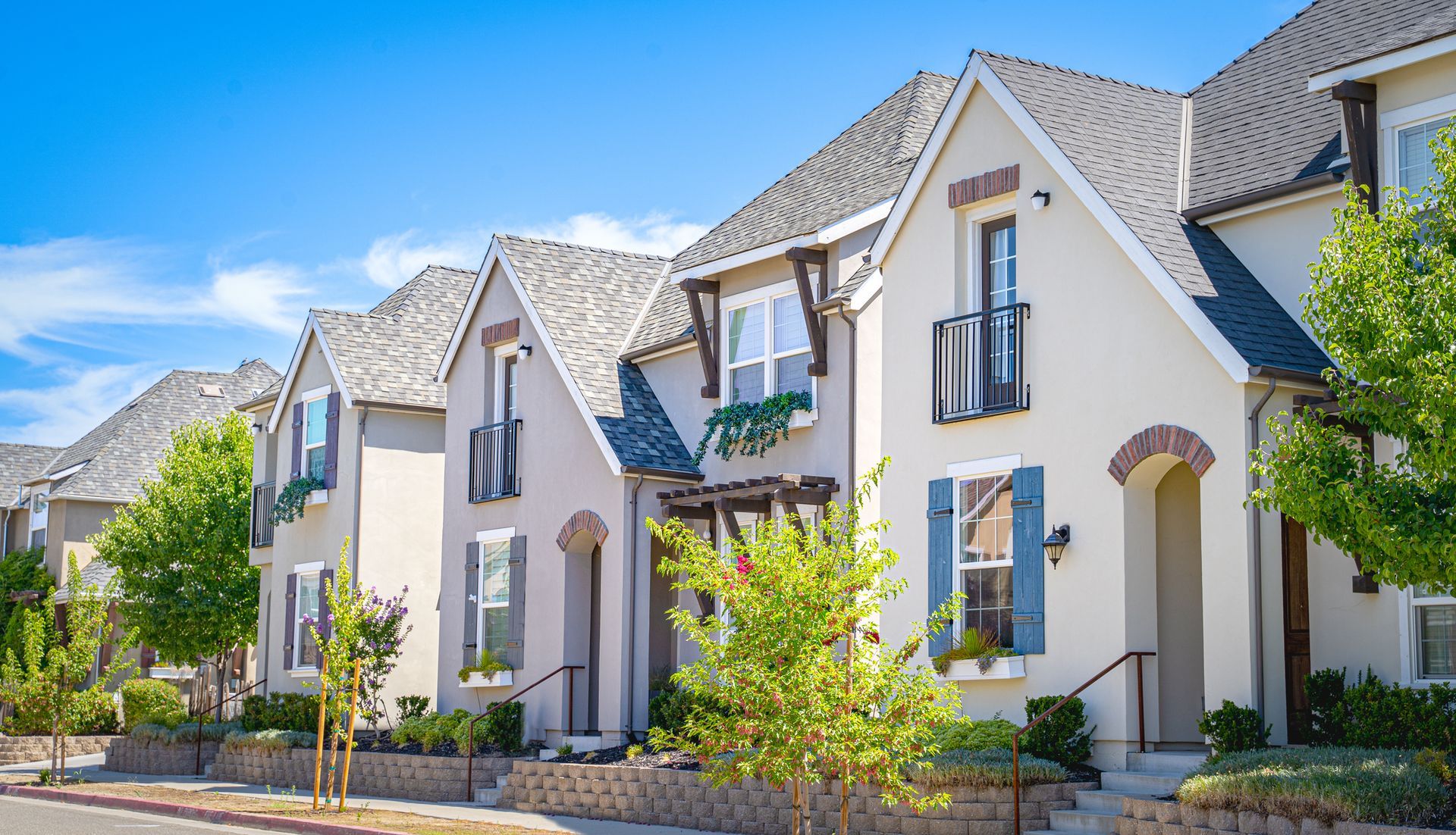 Row of modern white townhouses with gray roofs and small front gardens on a sunny street
