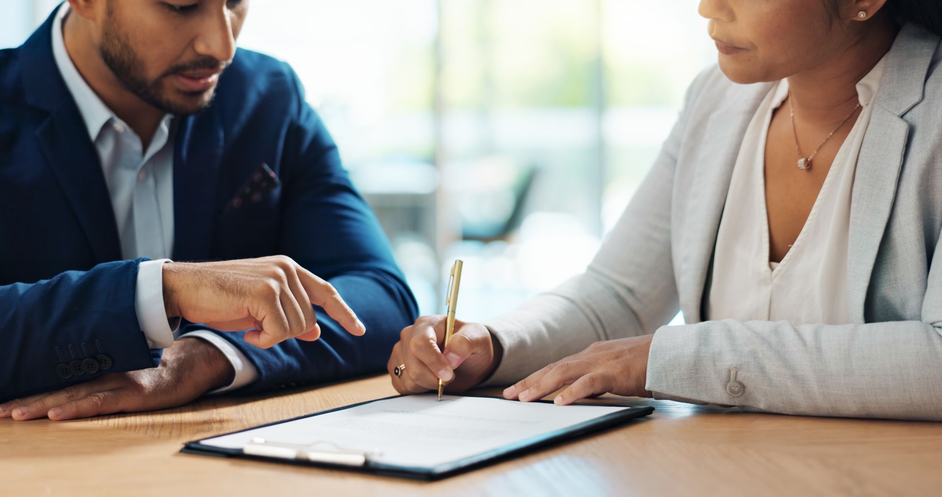 Two people reviewing a document at a table, one pointing and the other writing with a pen.