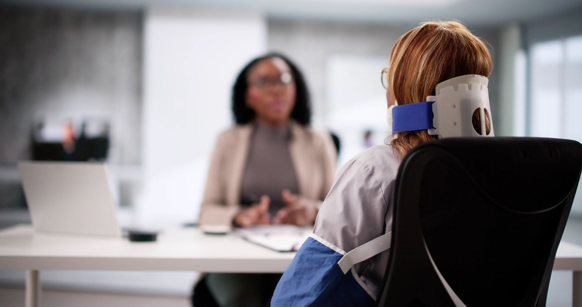 Person with blue neck brace speaking with clinician in a bright office room