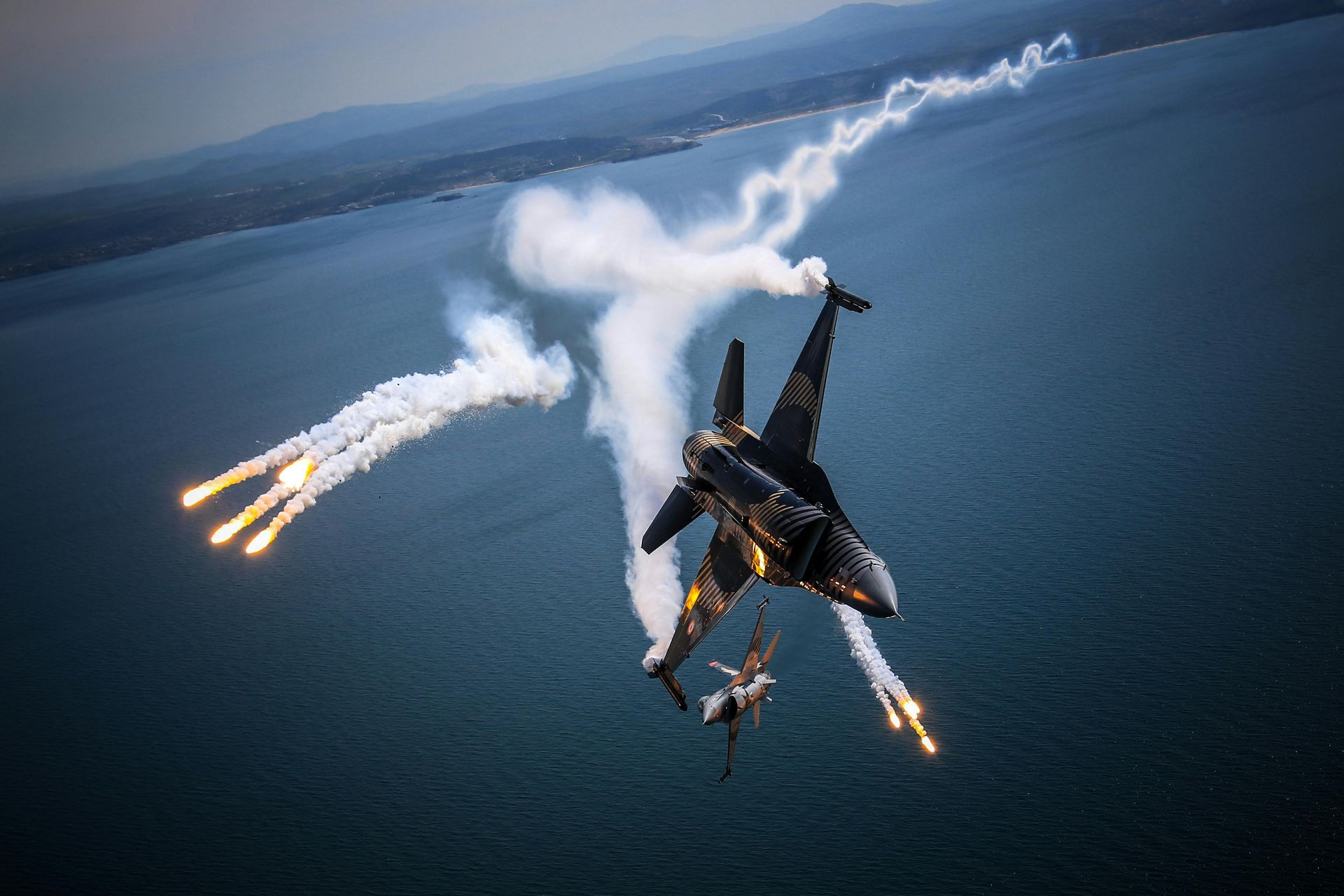 Two jets over the ocean in a dog fight. One firing off flares to avoid missile lock