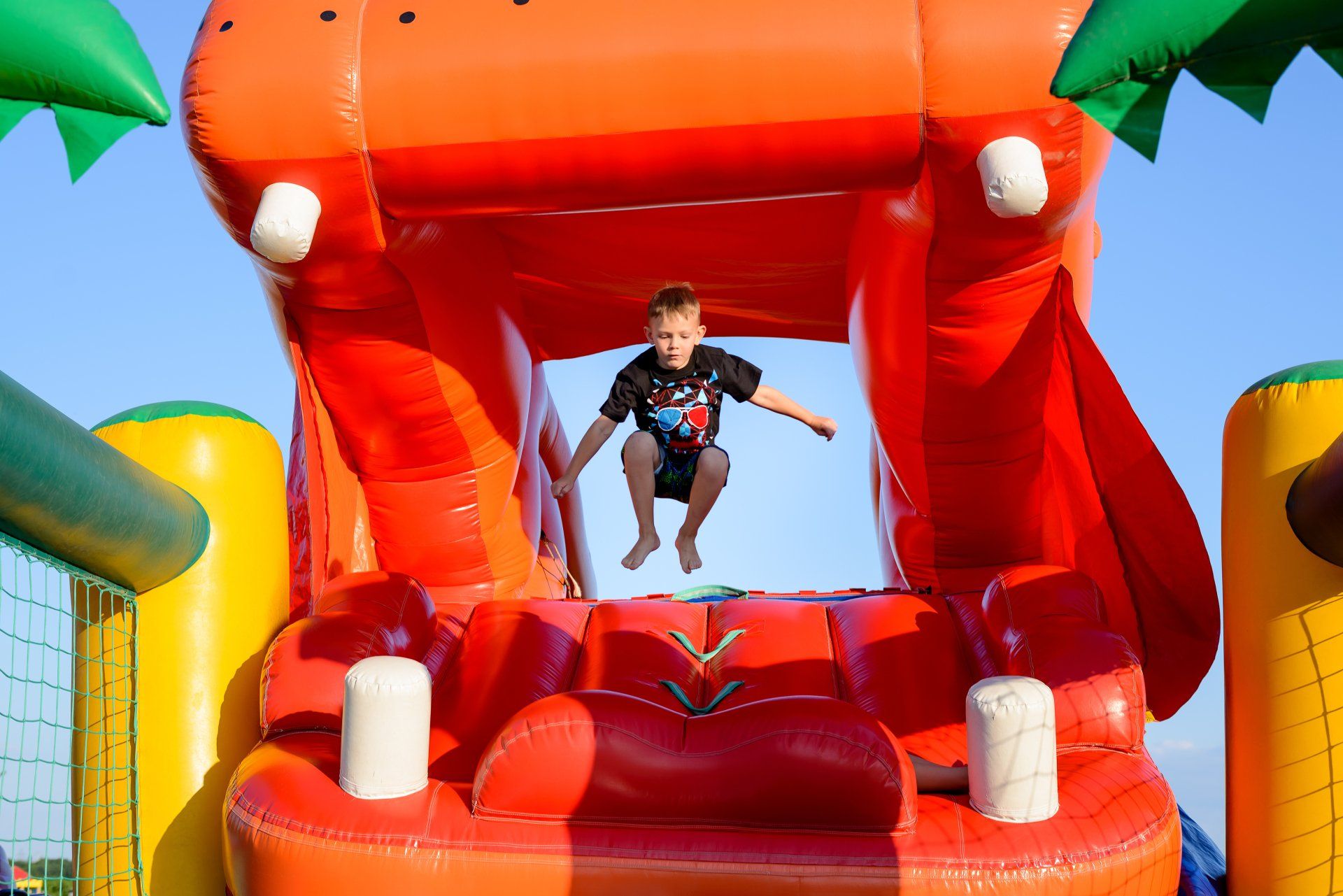 Small boy (6-8 years) wearing t-shirt and shorts jumping bare foot in the air on a colorful bouncy castle