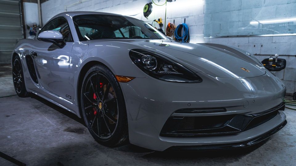 A gray porsche boxster is parked in a garage.