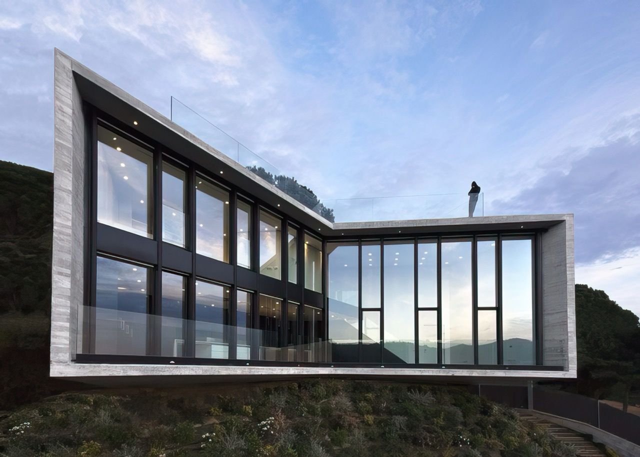 A modern house with a lot of windows is sitting on top of a hill.