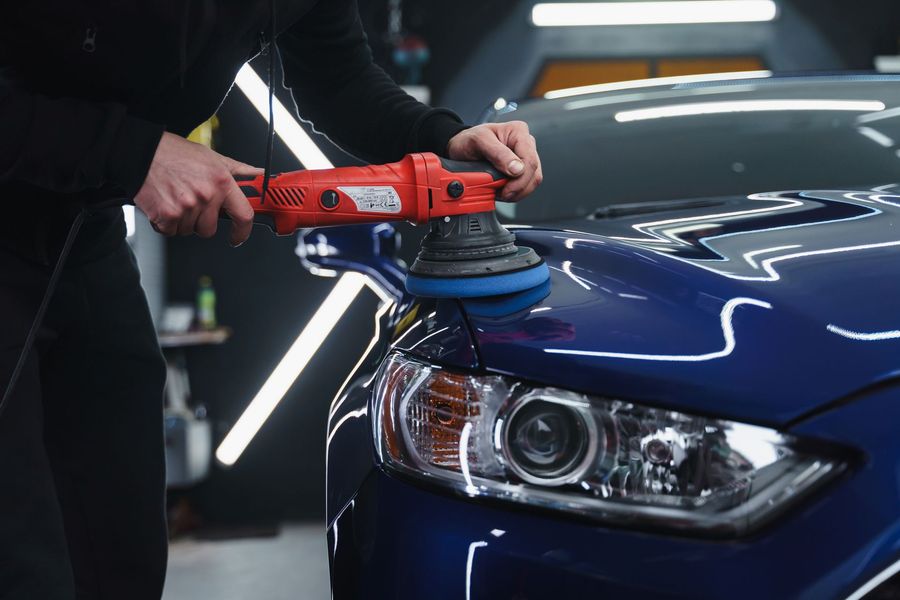 A man is polishing a blue car with a machine.