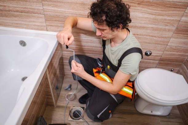 A man is kneeling down in a bathroom next to a toilet and bathtub.