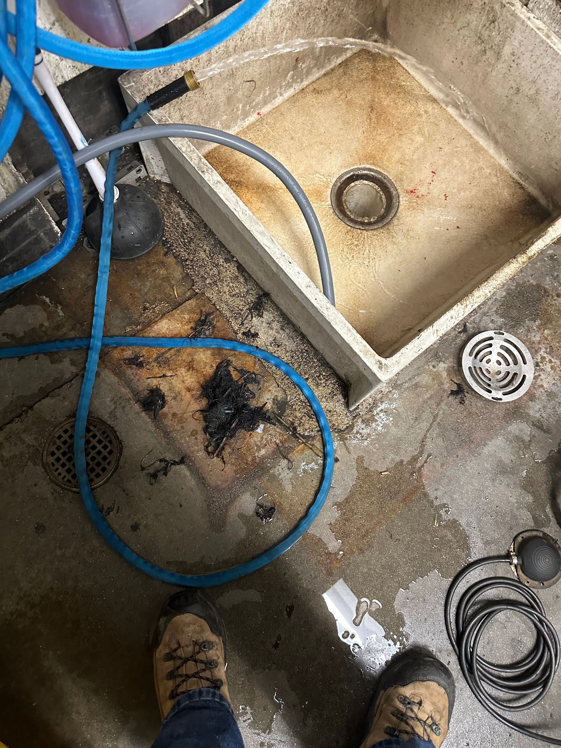 A person is standing next to a dirty sink with a hose attached to it.
