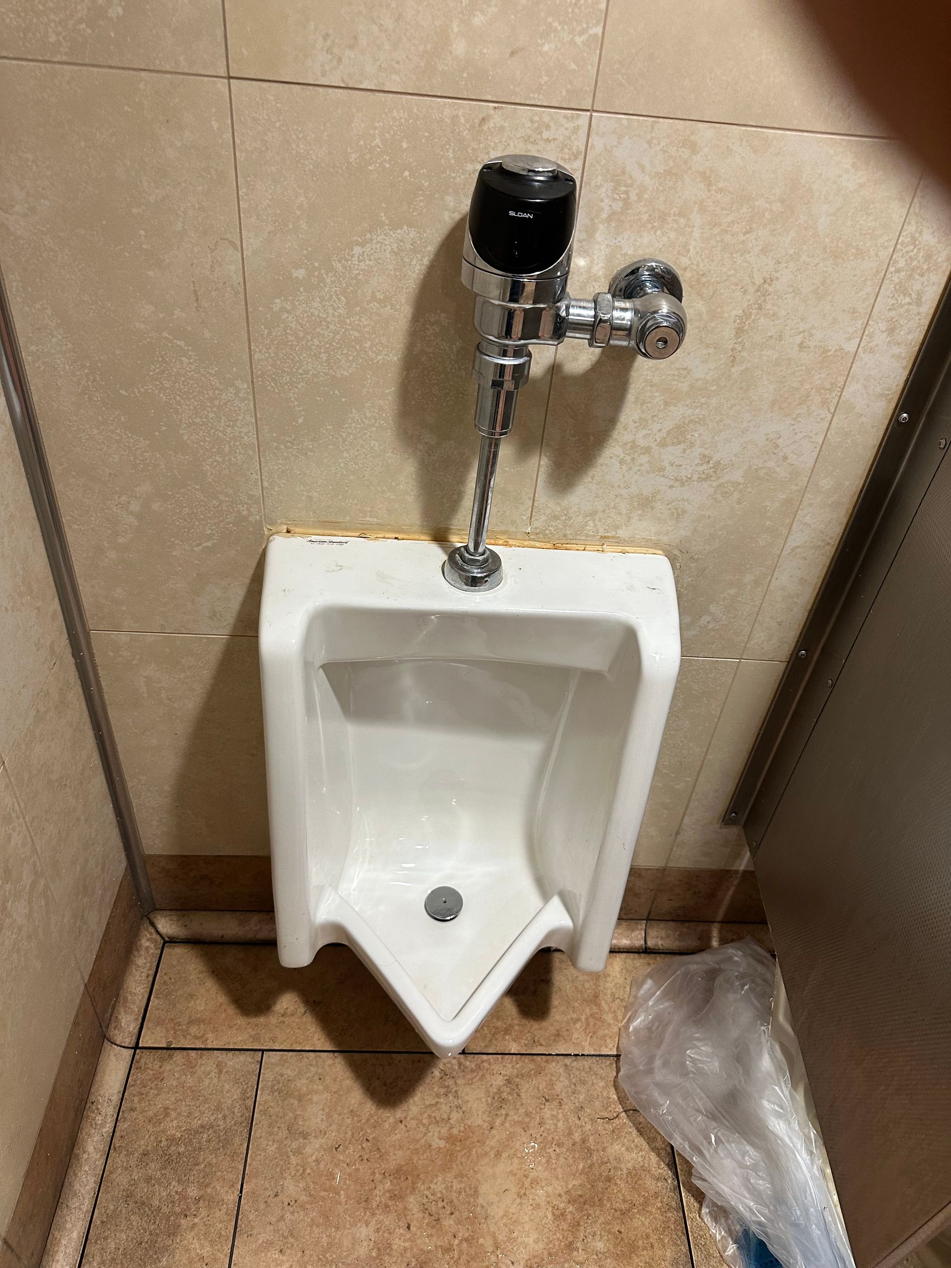 A white urinal is sitting in a bathroom next to a trash can.
