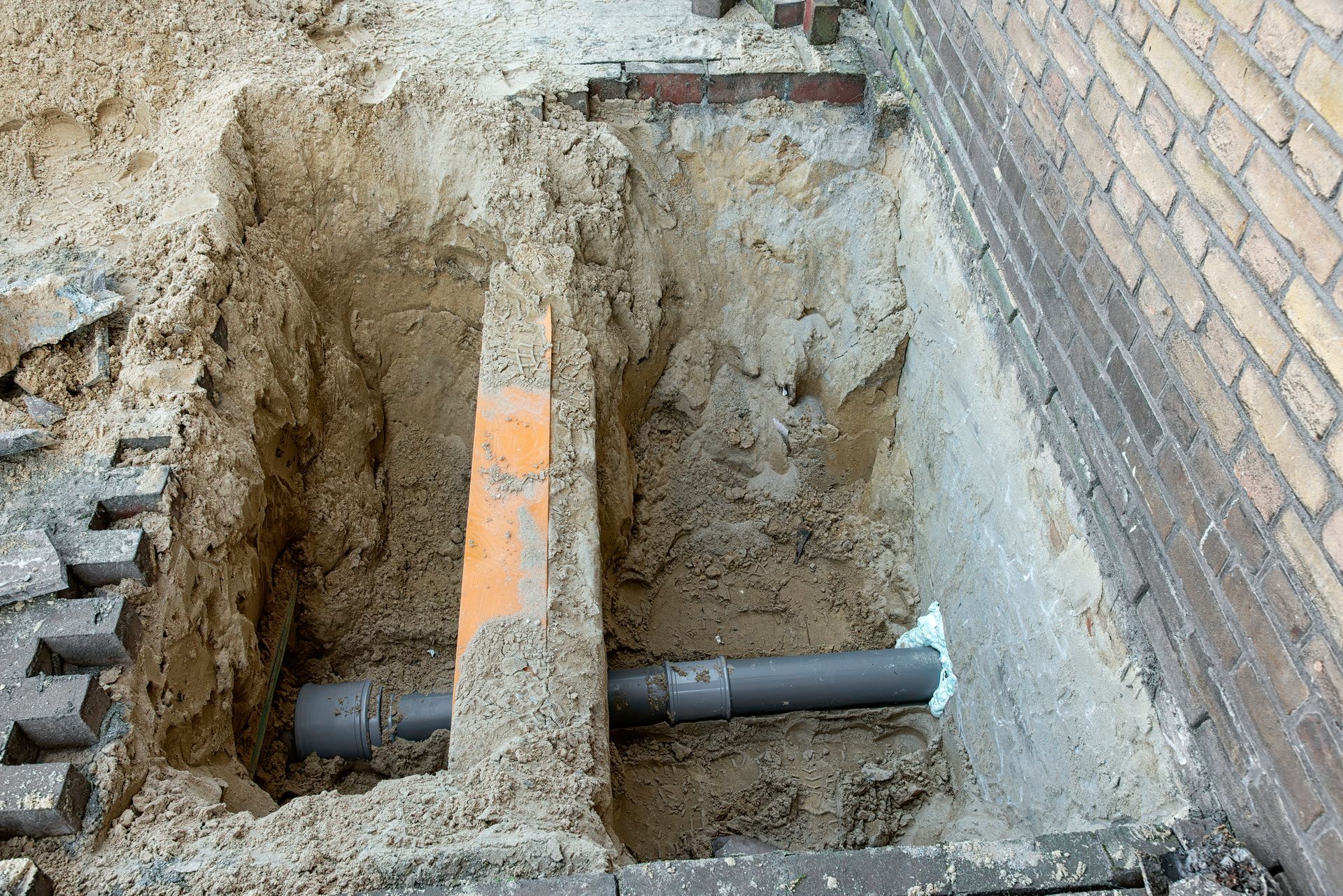 A pipe is being installed in a hole in the ground next to a brick wall.