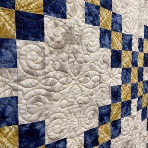 A close up of a blue and yellow quilt on a wall.