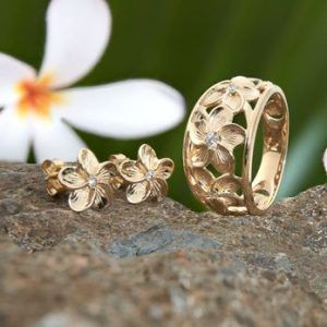 A ring and earrings are sitting on a rock with a flower in the background.