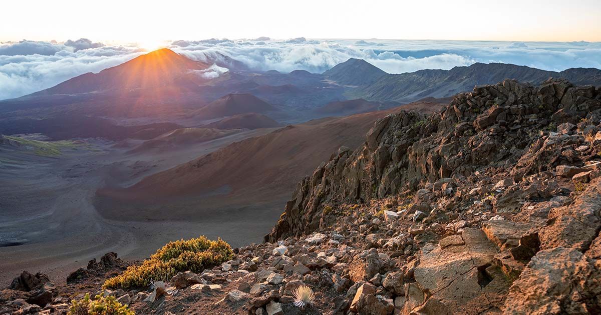 Sunrise view above the clouds from the summit of Haleakalā National Park on Maui, showcasing volcanic landscapes and clear skies during the dry season.
