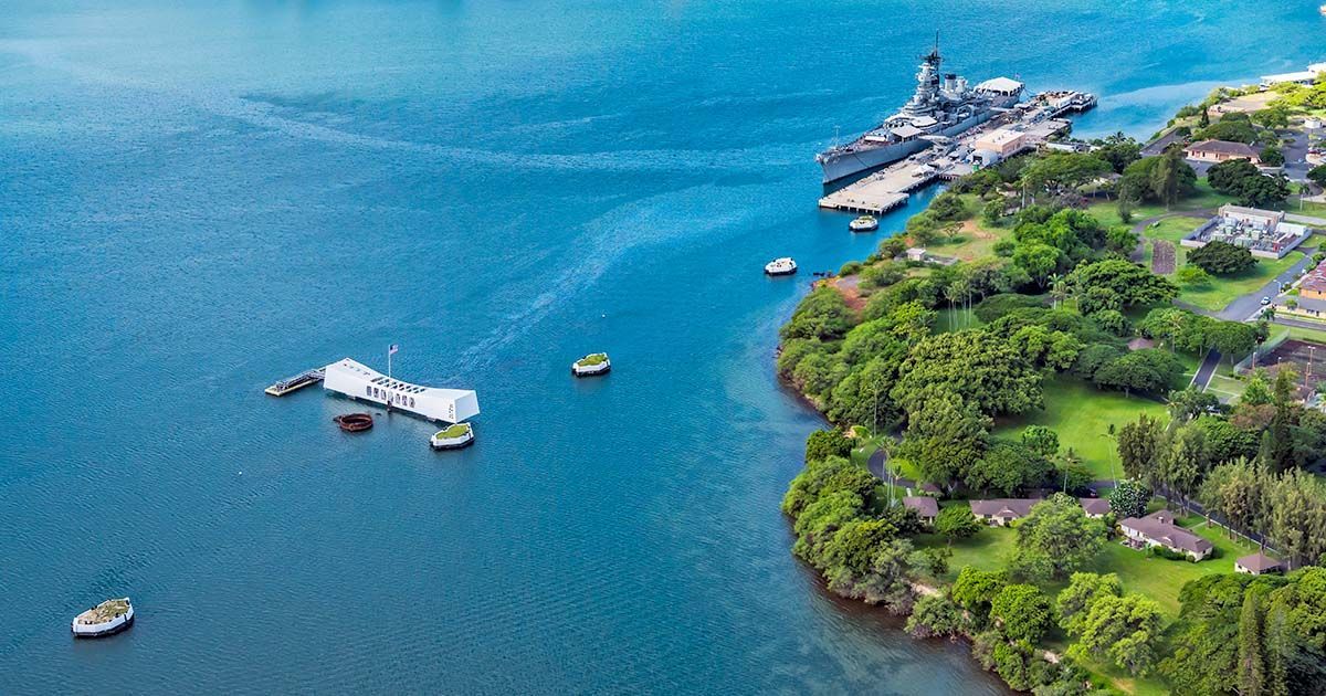 USS Arizona Memorial at Pearl Harbor National Memorial in Oahu, with white structure spanning the sunken battleship in calm harbor waters.
