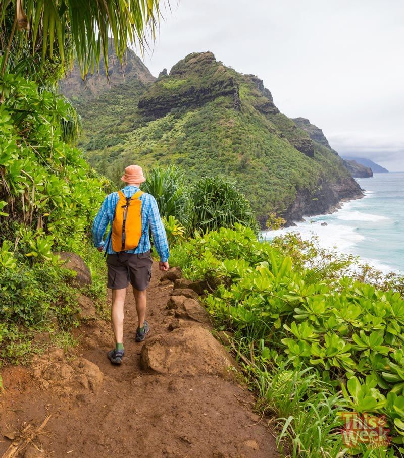 A man with an orange backpack is walking down a trail.