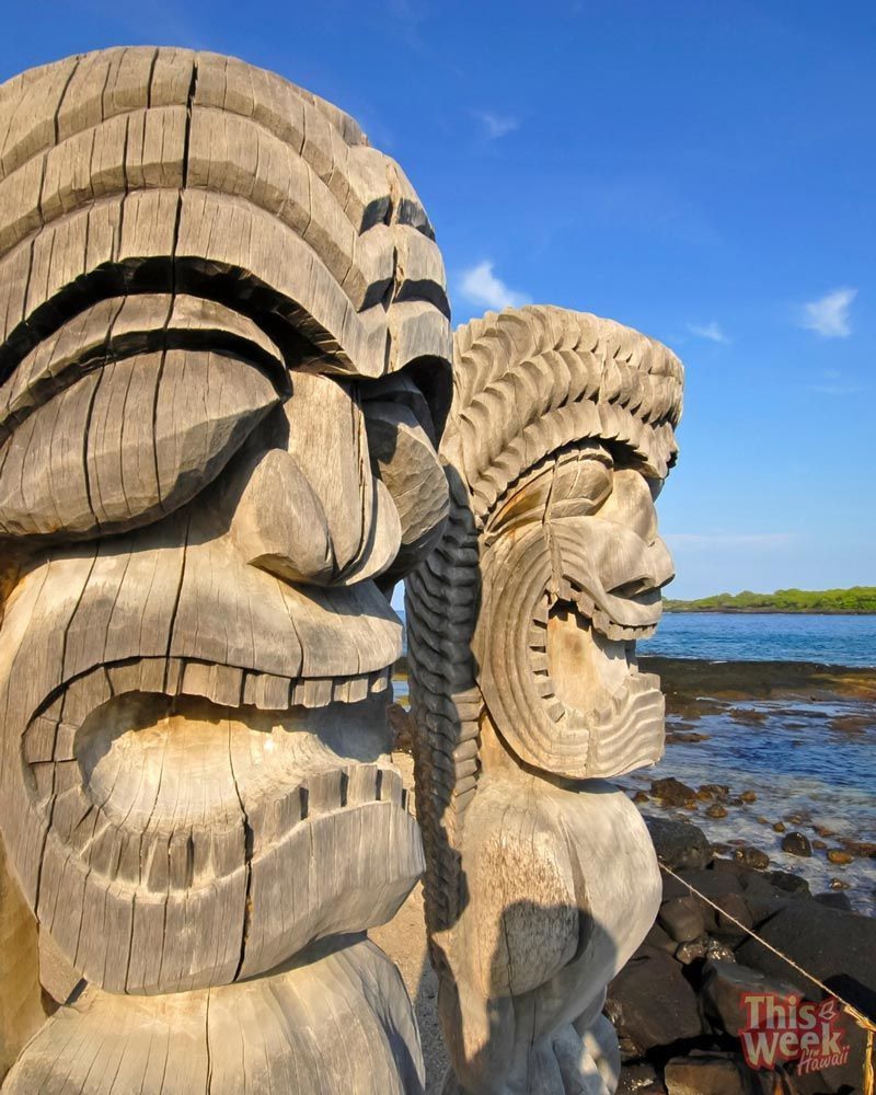Two tiki statues are standing next to each other in front of a body of water.