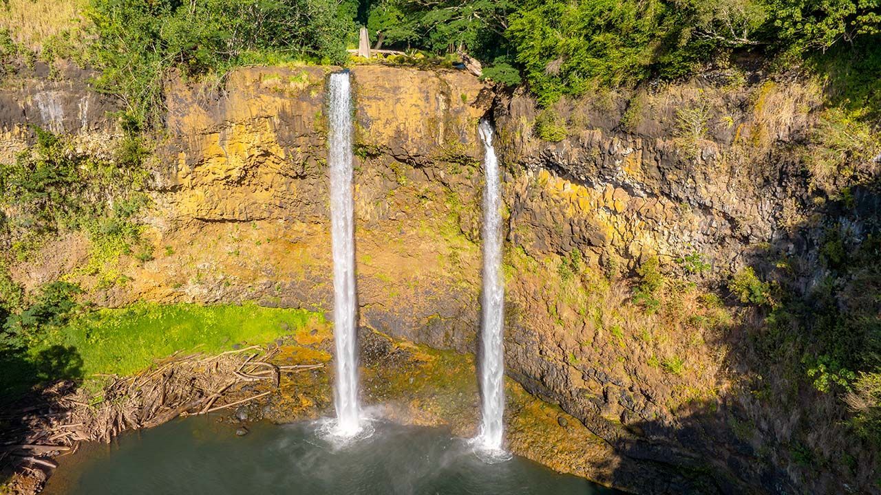 Wailua Falls on Kauai, Hawaii — a dramatic twin waterfall cascading 80 feet into a lush, tropical pool, seen from the roadside lookout near Lihue.