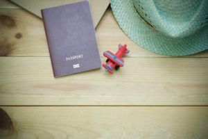 A passport , hat , and toy airplane are on a wooden table.