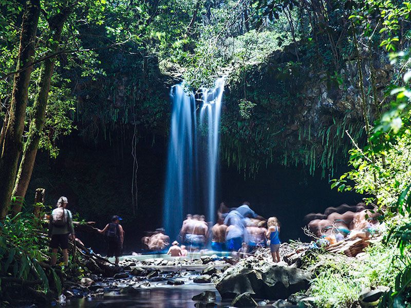 A group of people are standing in front of a waterfall.