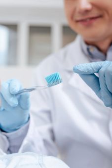 Manos enguantadas sosteniendo un cepillo de dientes con cerdas azules en un entorno de bata de laboratorio.