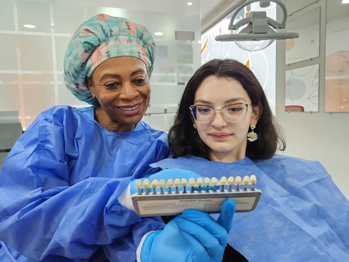Dos profesionales dentales con batas azules examinan una hilera de modelos de dientes en una clínica.