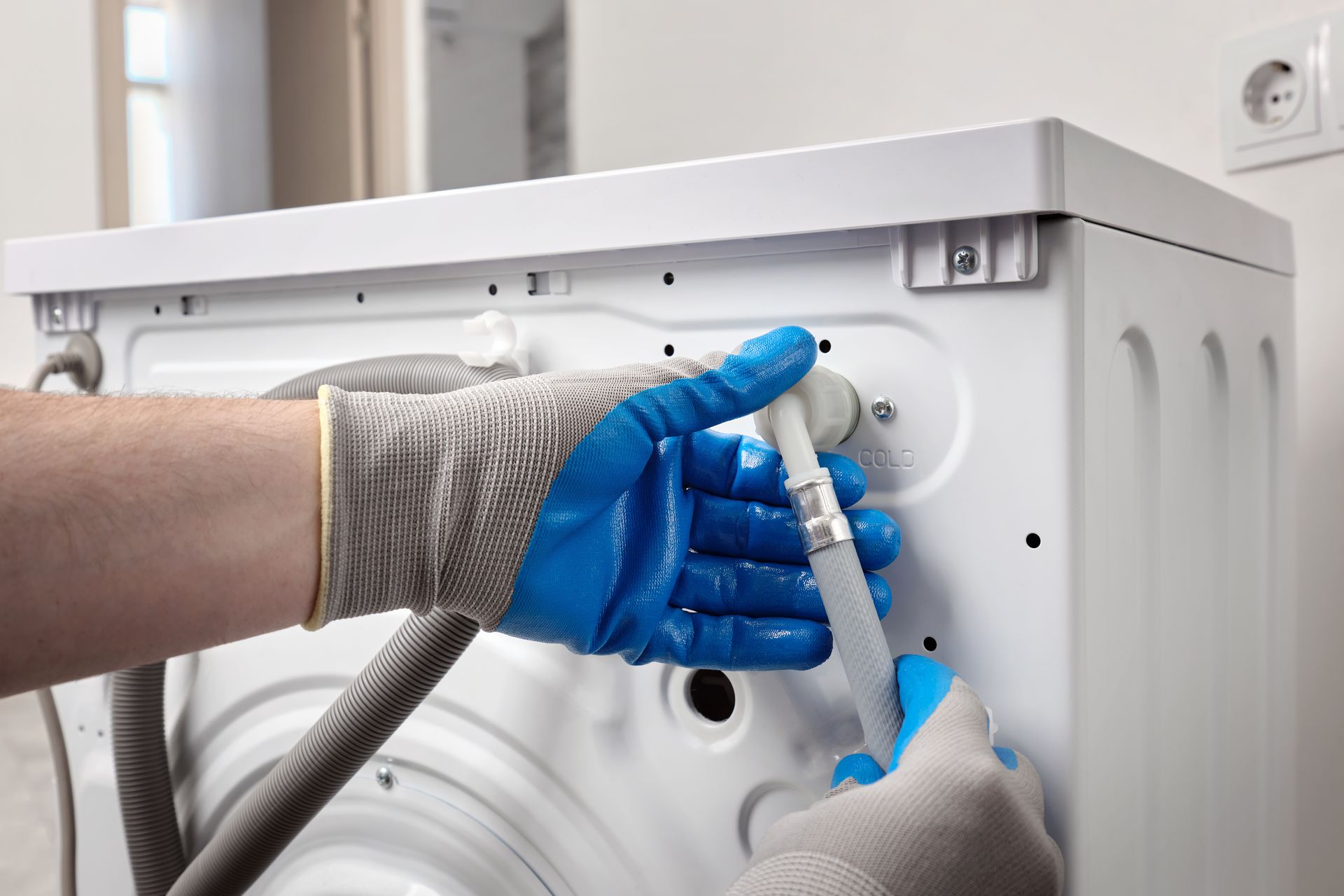 Gloved hands connecting a washer hose to the back of a washing machine