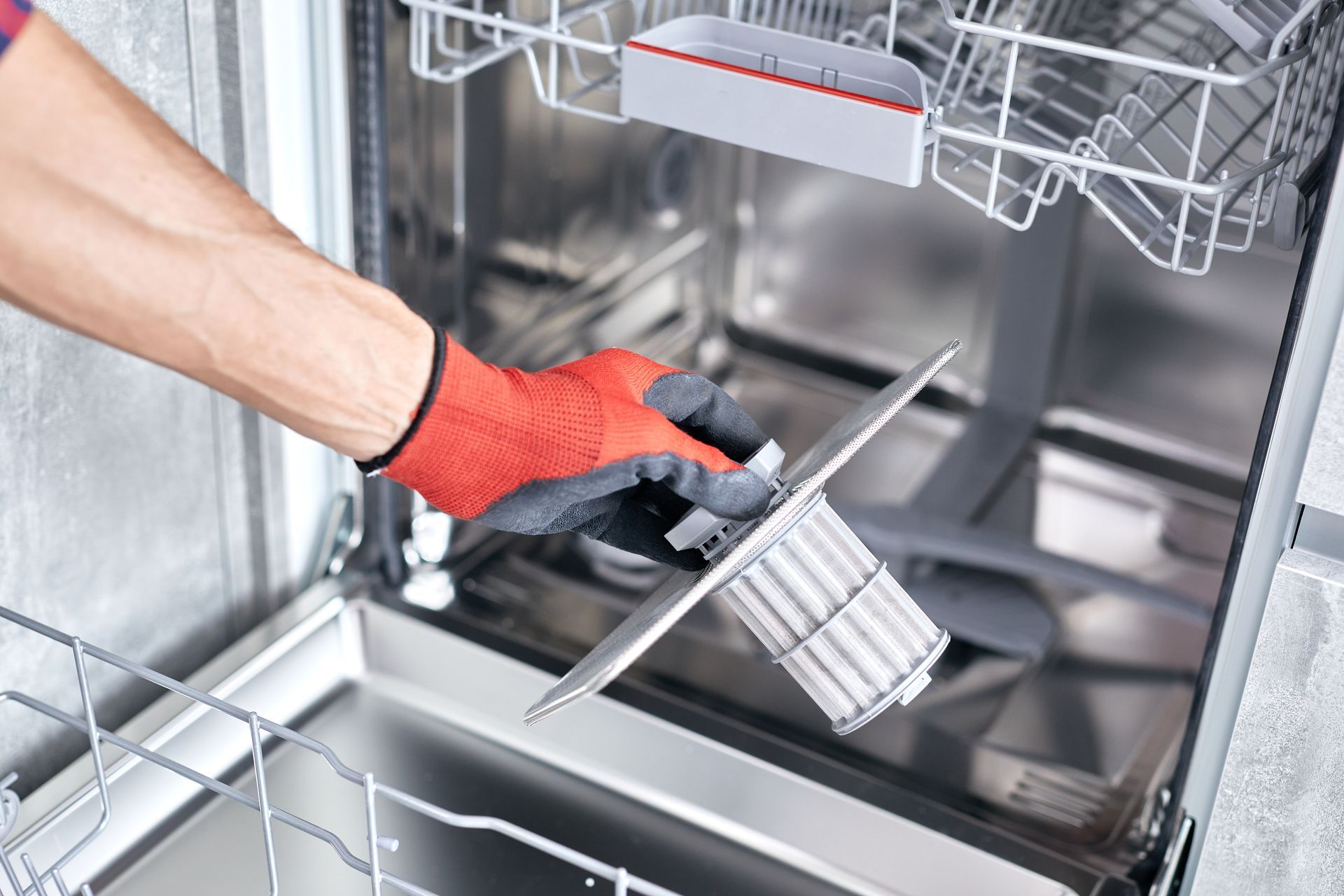 Gloved hand cleaning a dishwasher interior with a brush and spray bottle