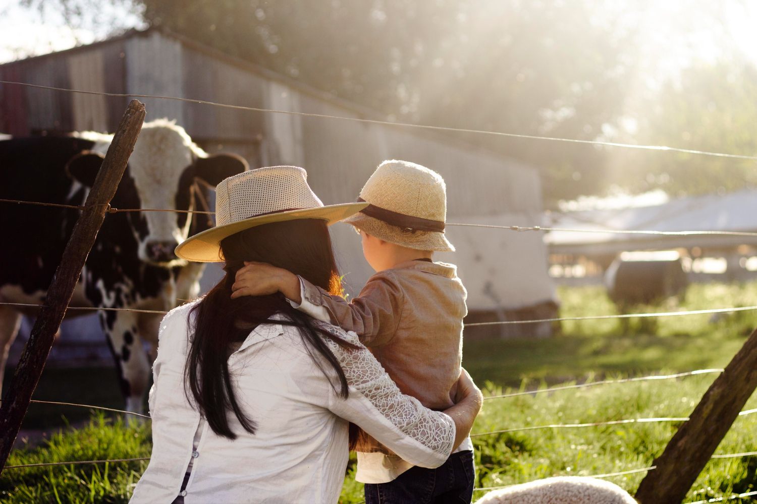 A woman is holding a child in front of a cow in a field.