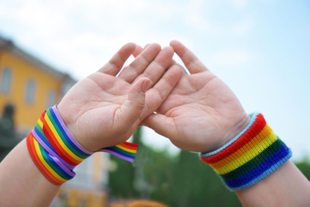 Two people wearing rainbow wristbands are giving each other a high five.